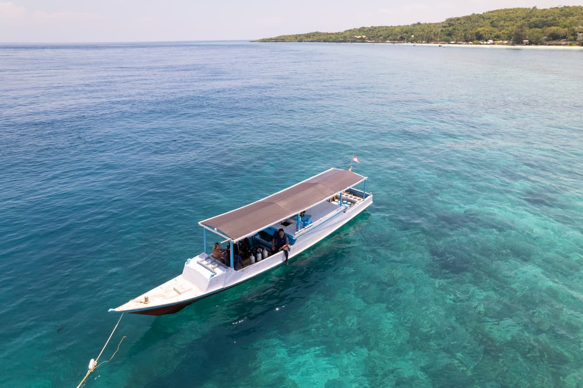 A white wooden dive boat on its mooring over the reef, tanks and divers under the canopy