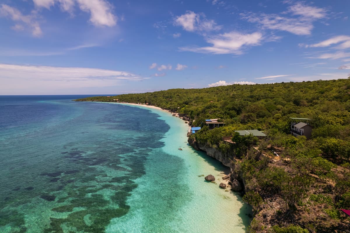 Bara Beach from above in daylight: the cliff, the curve of white sand and the reef