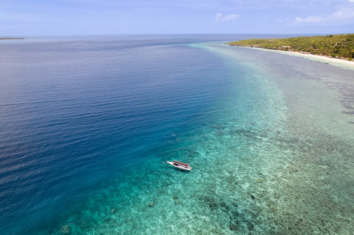 A small boat moored where the reef ends and deep blue water begins, the coast and a white beach in the distance